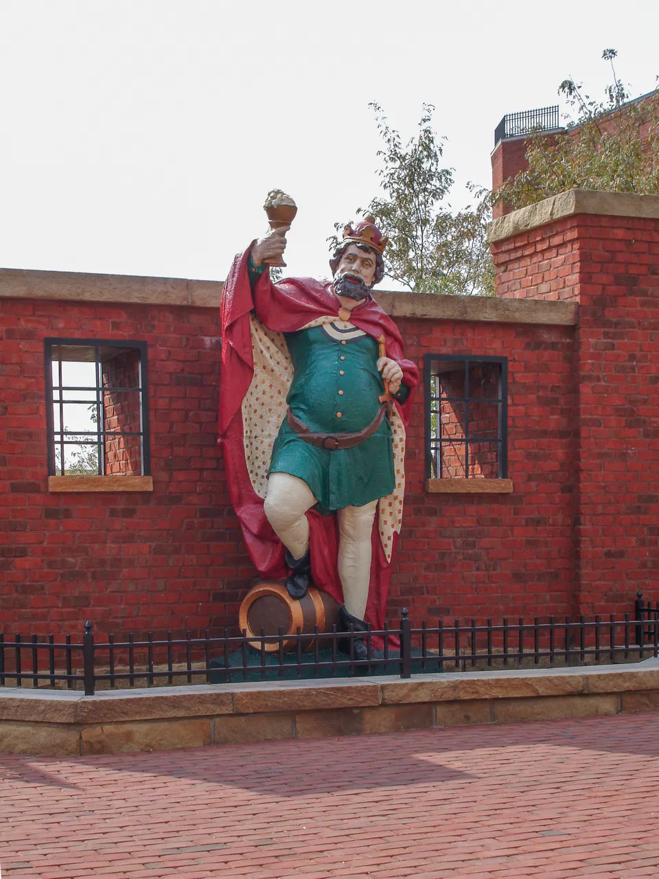 Public art figure set against brick buildings with low planting and courtyard paving.